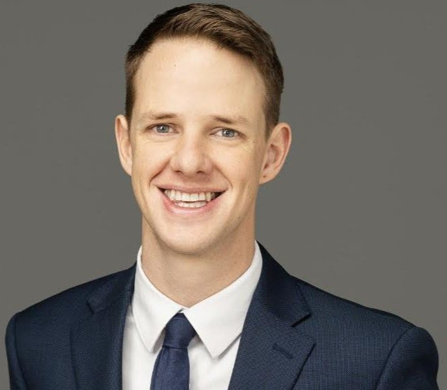 Smiling man in a navy suit and tie against a gray background