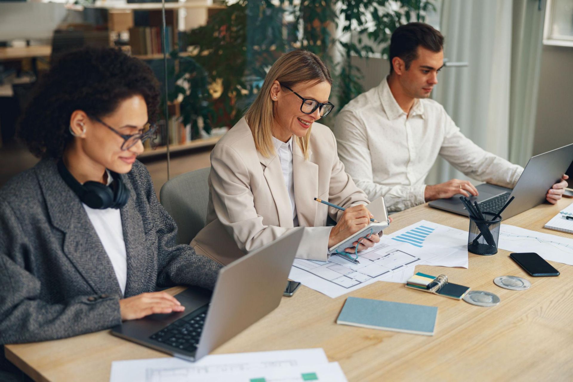 Three coworkers collaborating at a conference table with laptops and documents in a bright office