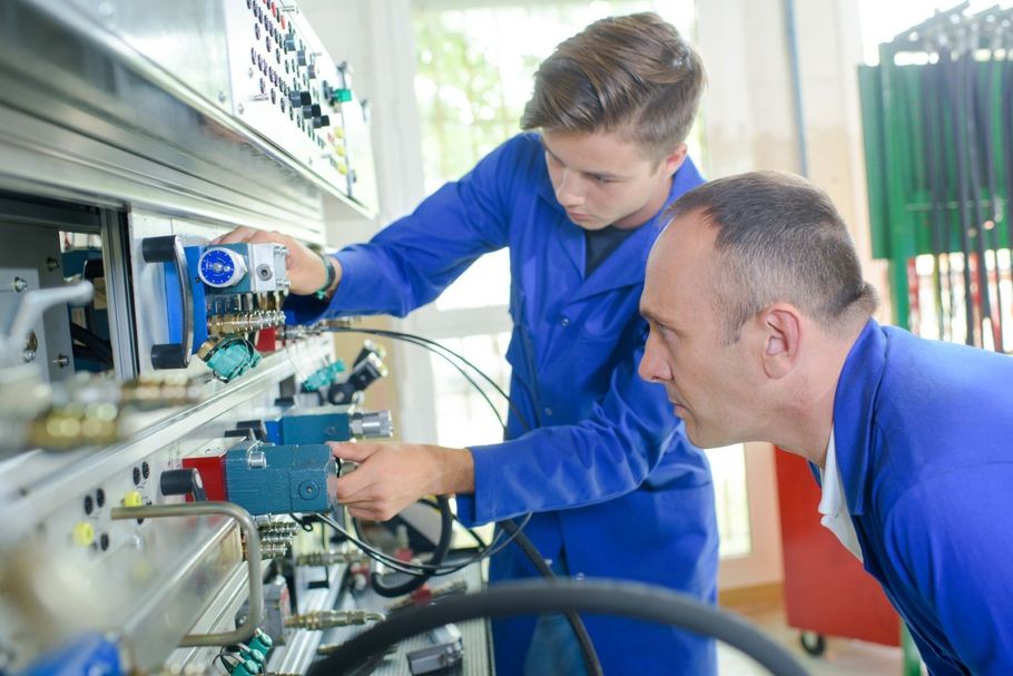 Two technicians in blue uniforms inspect machinery in an industrial workshop