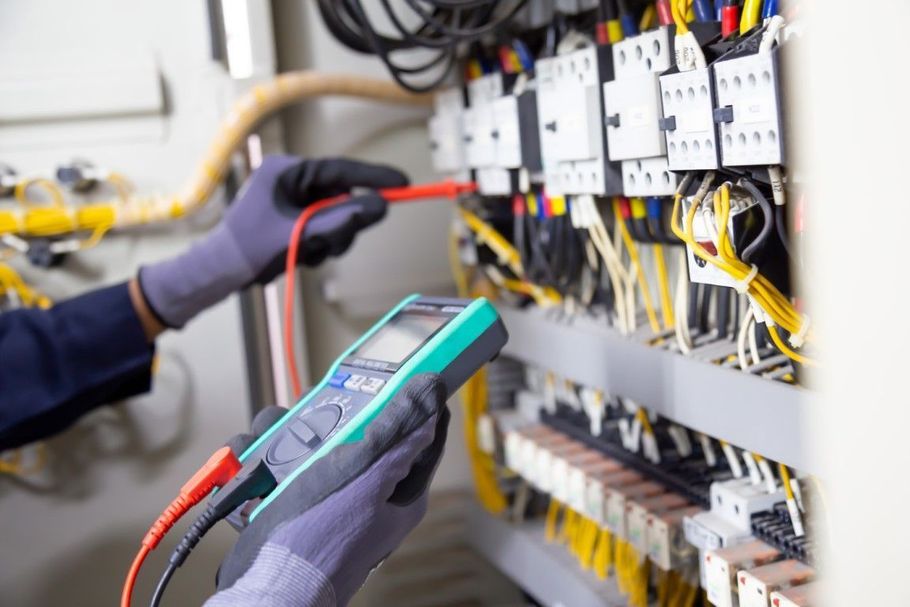 Technician testing electrical control panel with a digital multimeter and gloved hands