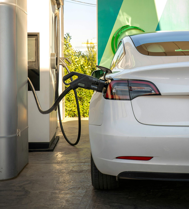 White electric car plugged into a charging station outdoors, rear view with cable connected