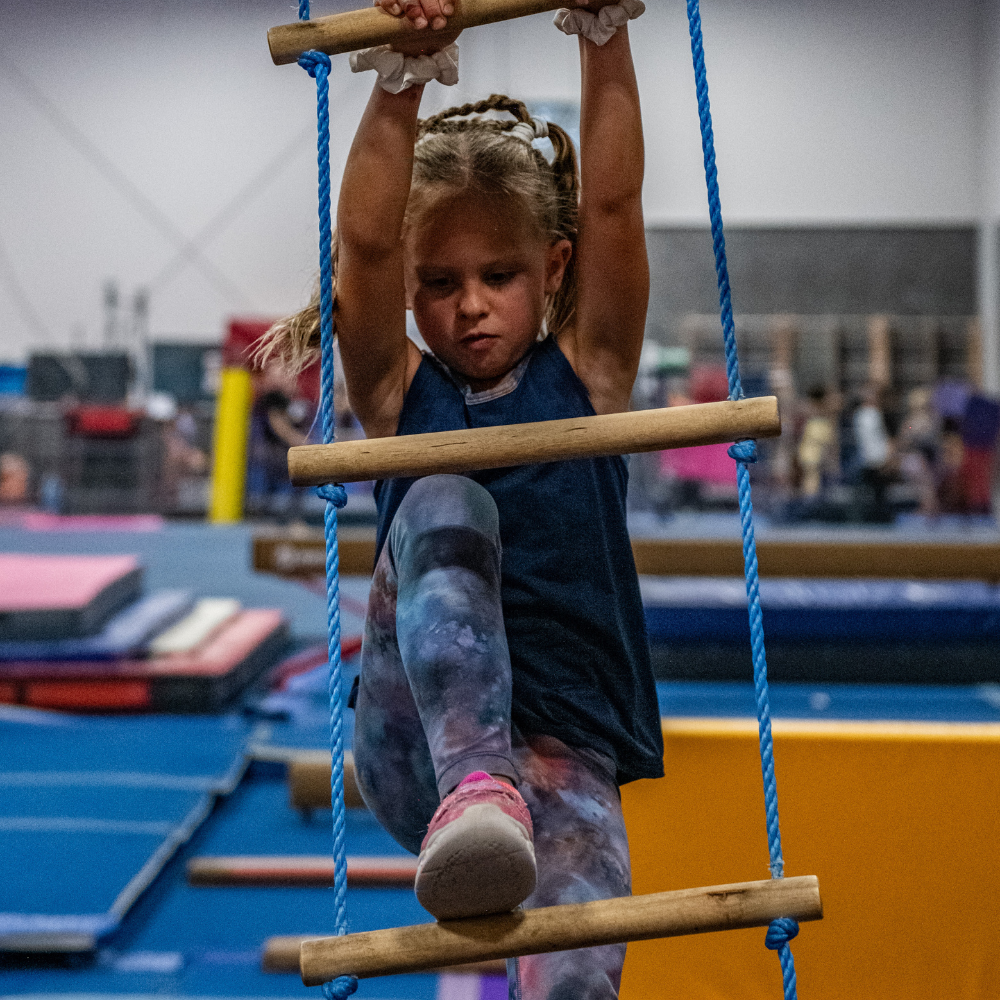 A little girl is climbing a wooden ladder in a gym