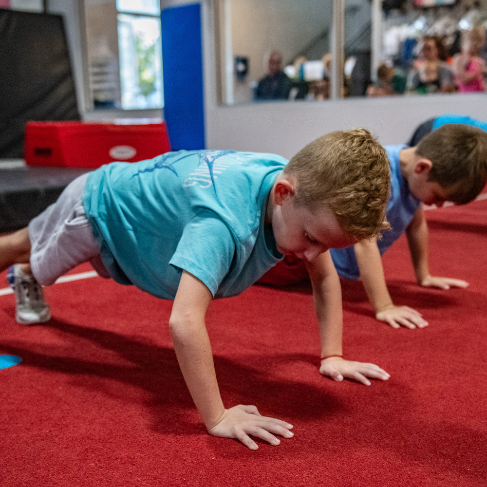 Two young boys are doing push ups on a red carpet