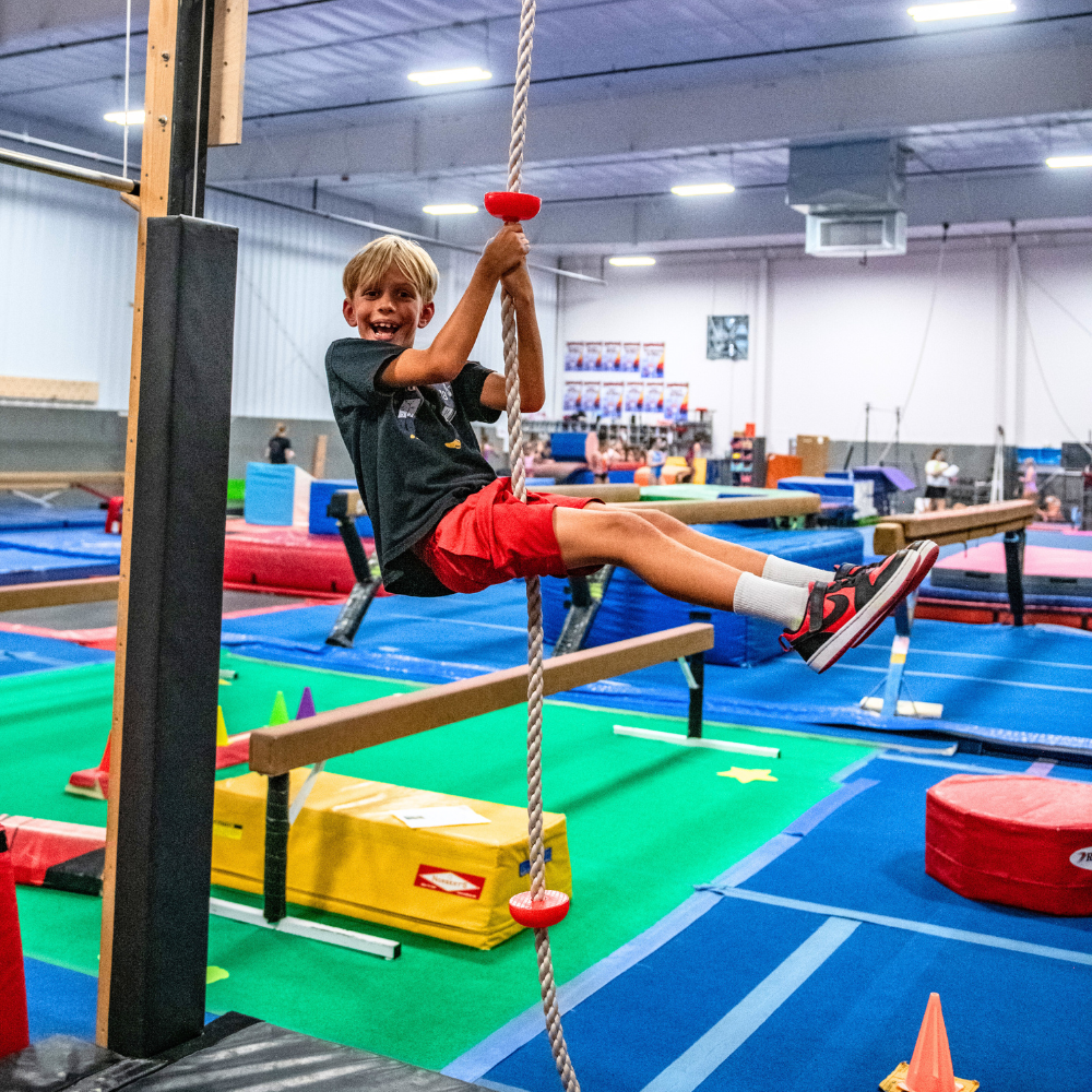 A young boy is climbing a rope in a gym.