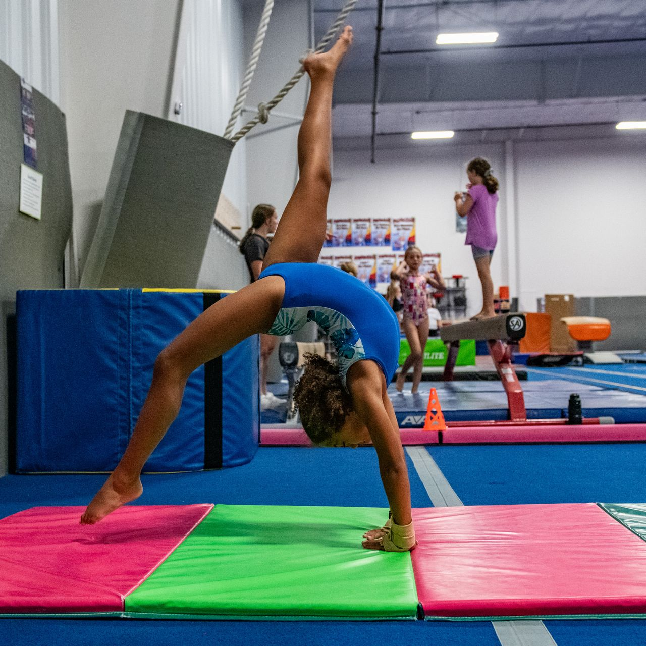 A tumbler is doing a bridge kick over on a panel mat