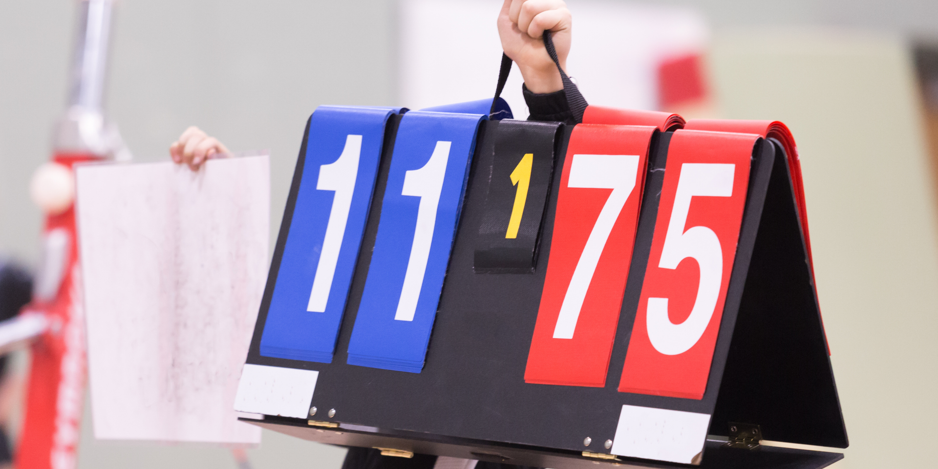 A gymnastics judge is holding a scoreboard that says 11 75