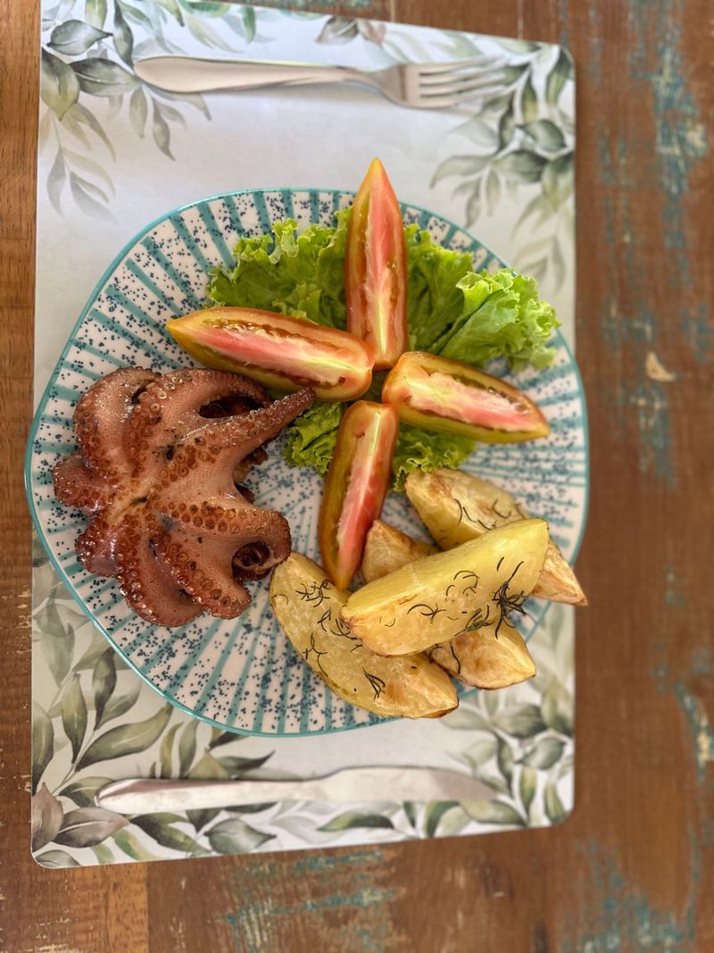 Tentáculos de polvo e frutas dispostos em um prato estampado com guarnição de alface.