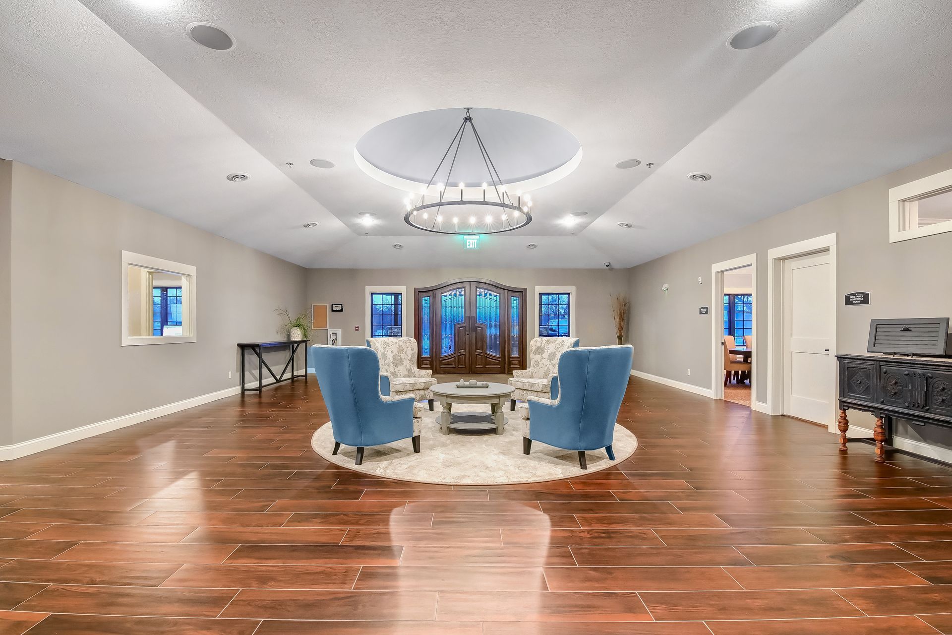 A large living room with hardwood floors , blue chairs , a piano and a chandelier.