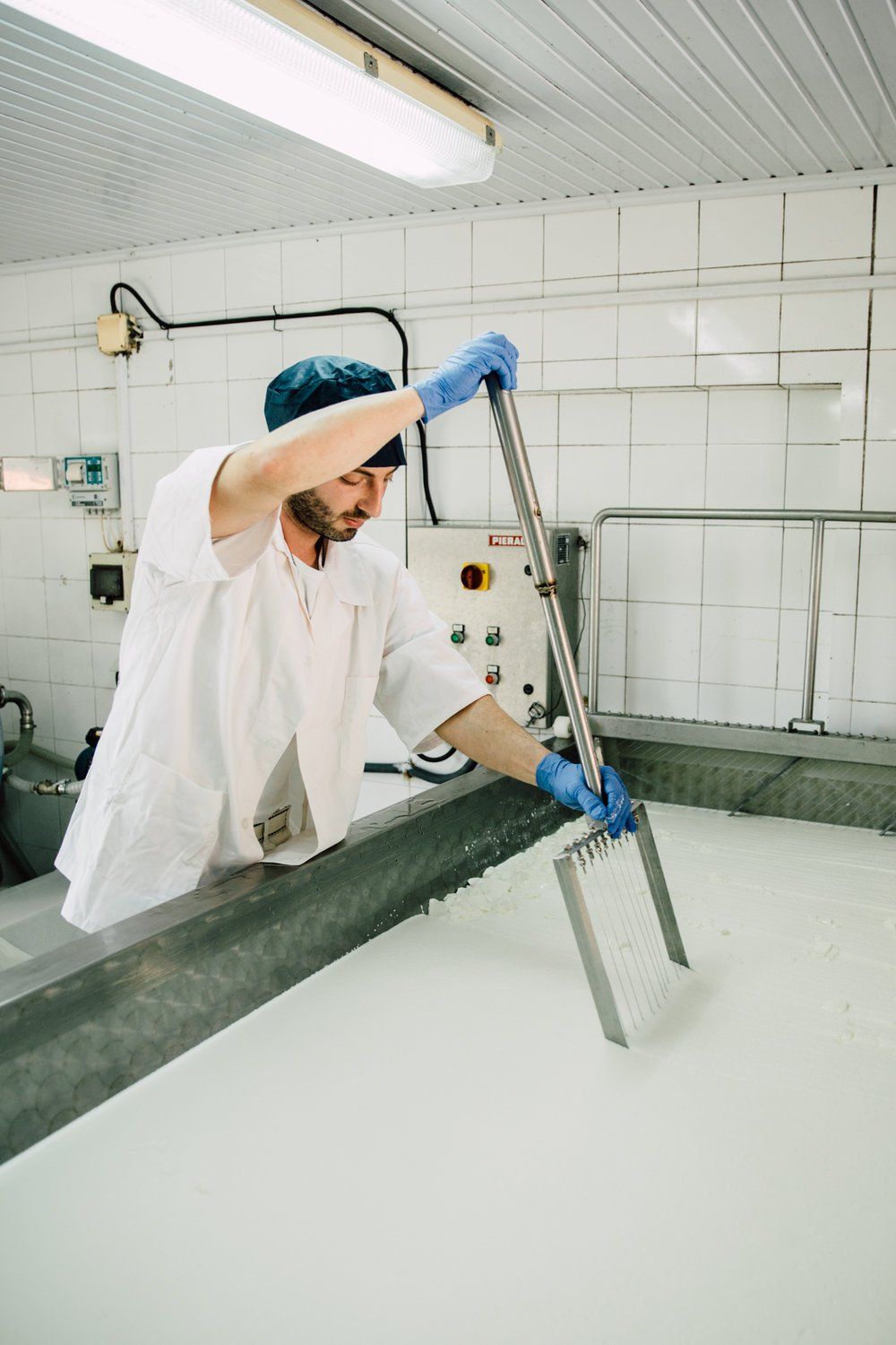 a man in a white coat and blue gloves is working in a factory .
