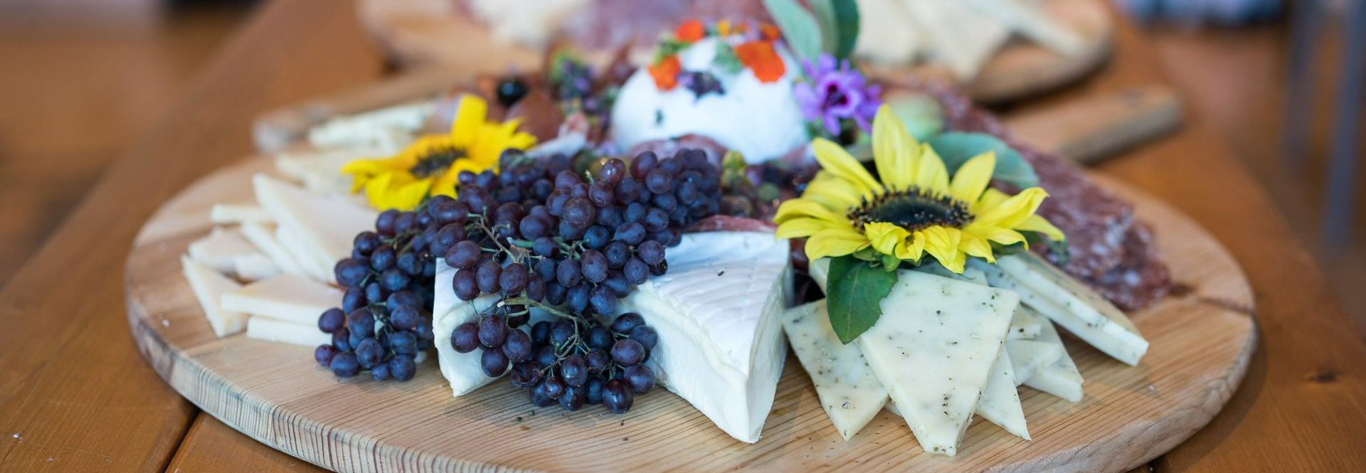 a wooden cutting board topped with cheese , grapes , and sunflowers .
