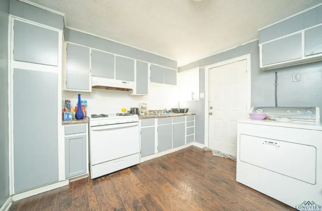 Three people in an empty room, one showing property to a couple. White walls, large window.