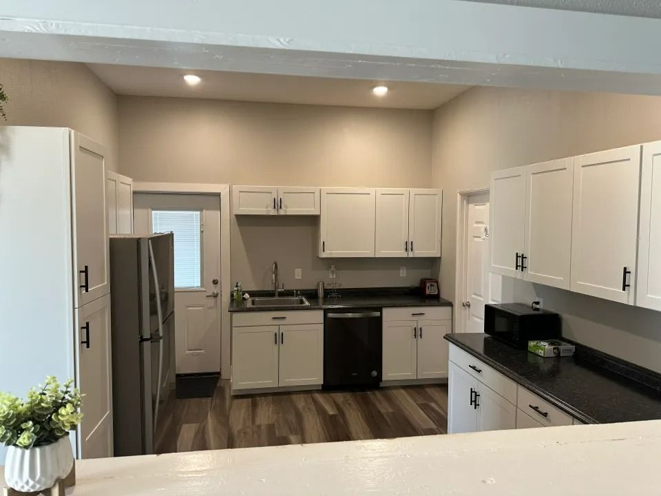 White kitchen cabinets with black countertops and appliances, wooden floor.