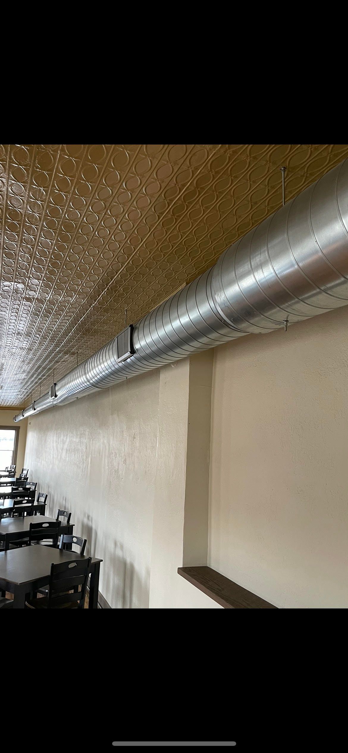 a restaurant with tables and chairs and a metal pipe hanging from the ceiling .