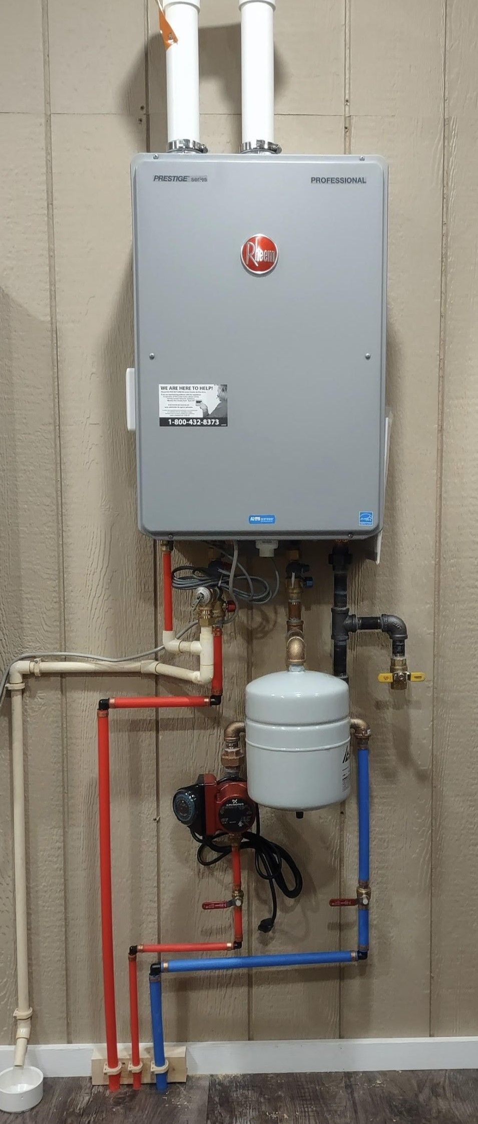 a water heater is hanging on a wall next to a bunch of pipes .