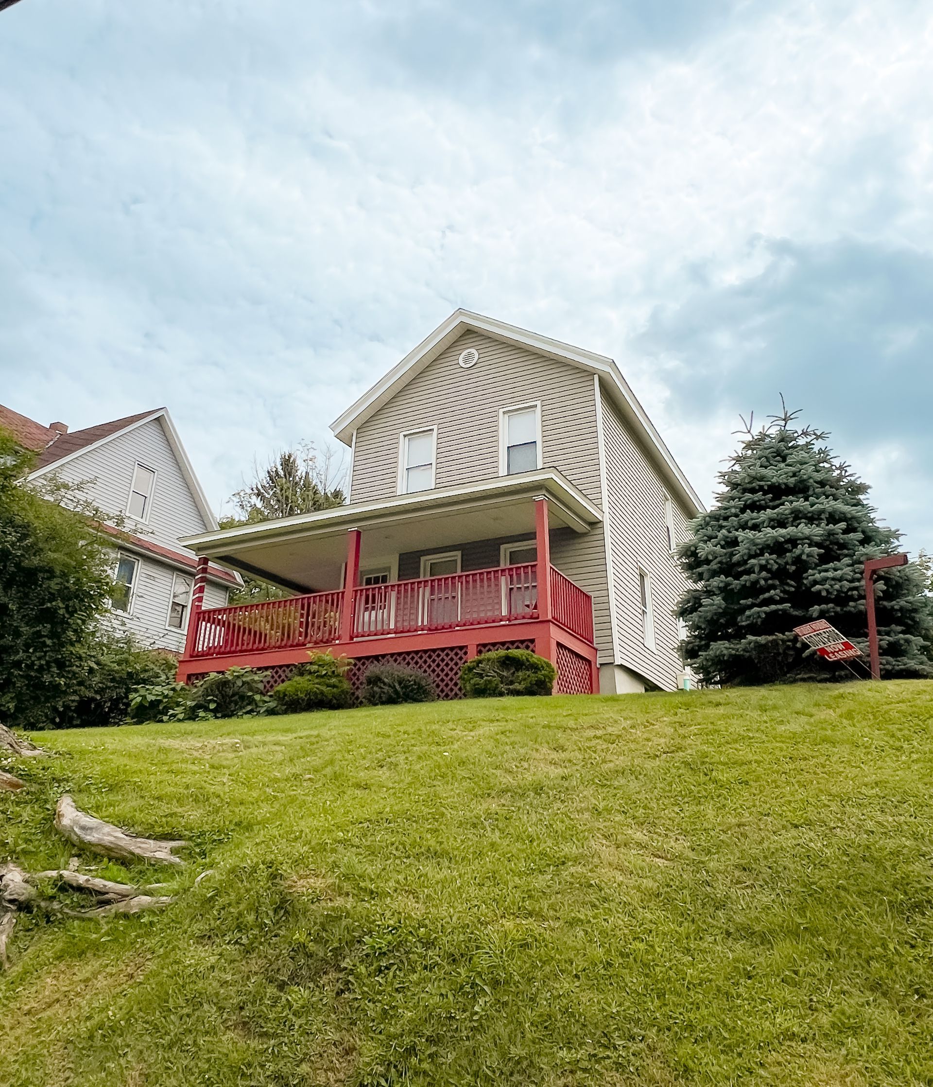 79 Groton – Beige two-story house with a red front porch, situated on a sloped grassy lawn.