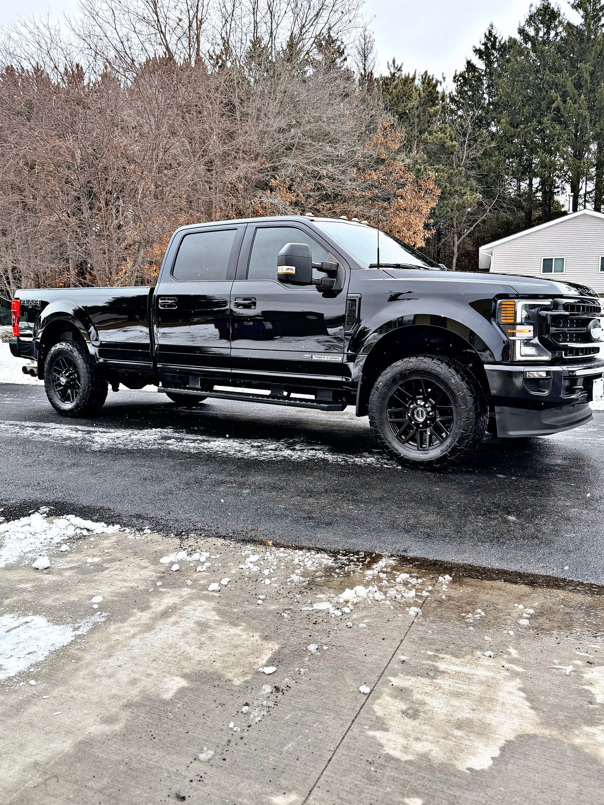 A black Ford F-Series pickup truck parked on a wet, light-dusted gravel lot.