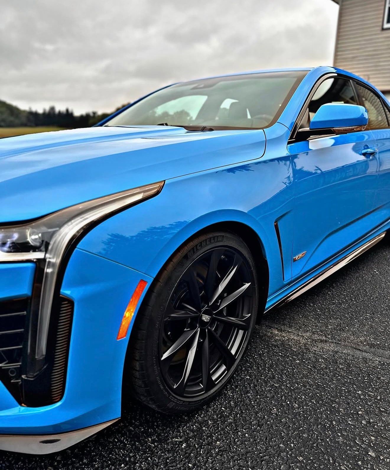 A vibrant blue Cadillac sedan is parked on an asphalt surface, showcasing its sharp headlights and sleek black wheels.