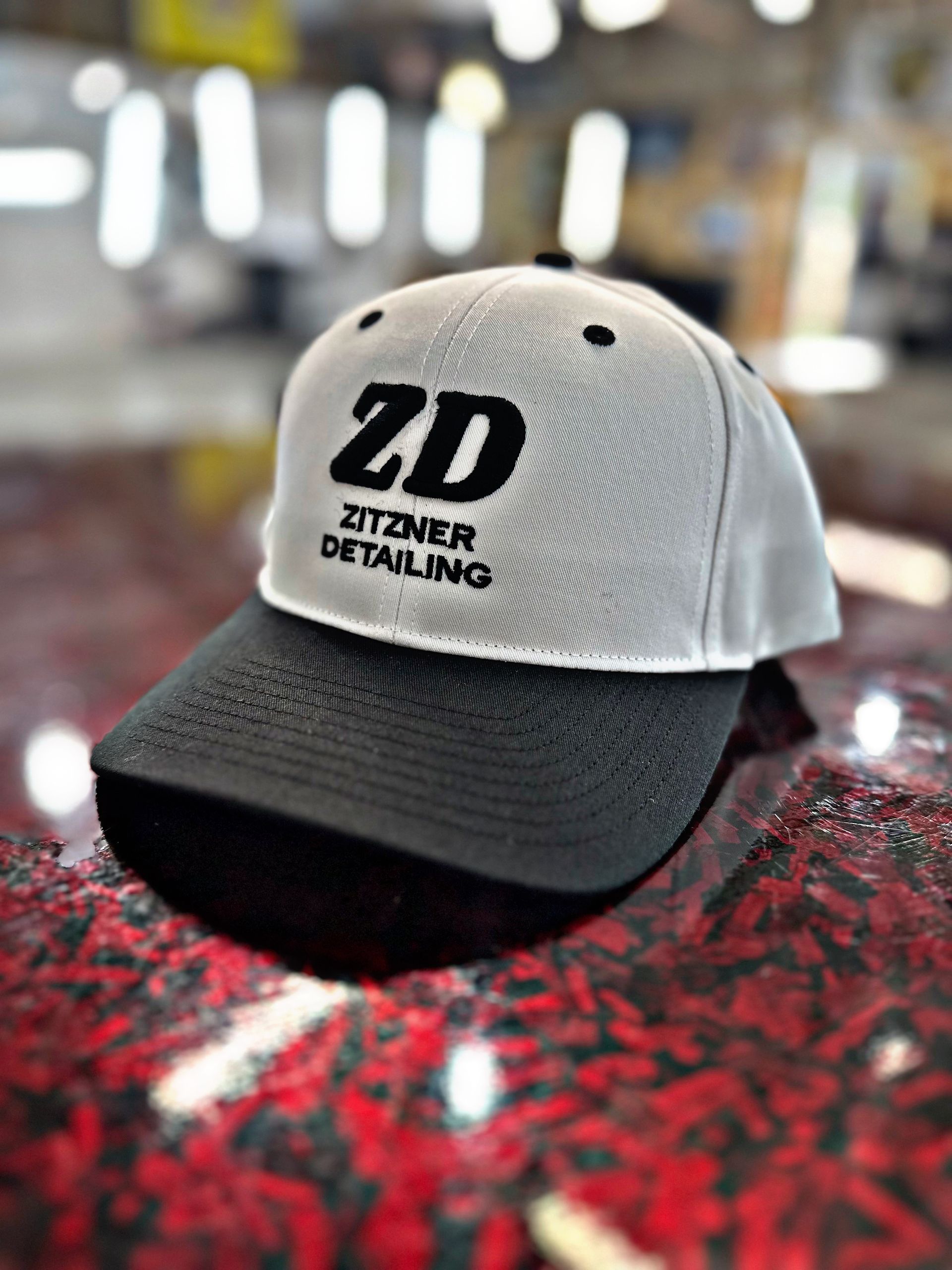 White and black Zitzner Detailing branded baseball cap resting on a red textured surface.