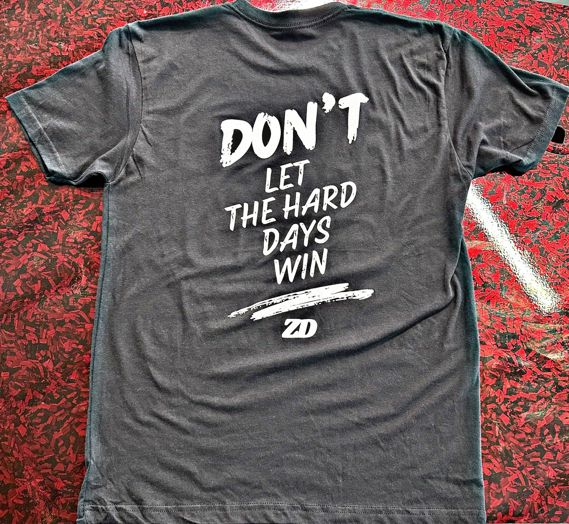 A gray heather T-shirt lying on a red textured surface, with the text 