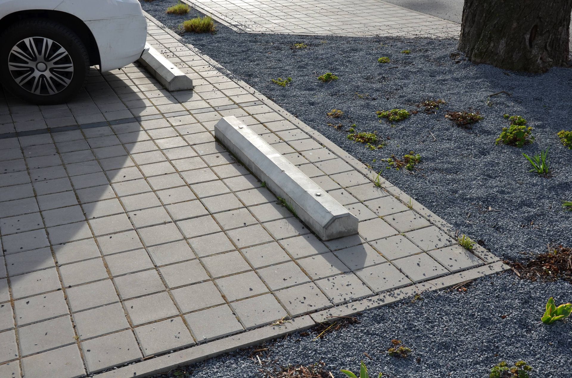 A white car is parked in a parking lot next to a concrete curb.