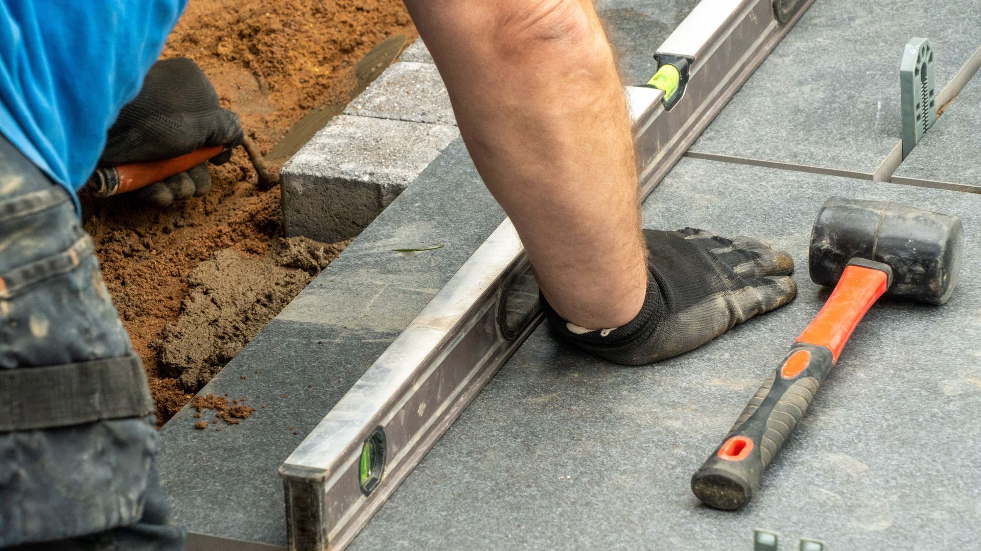 A man is using a level and a hammer to level a brick walkway.