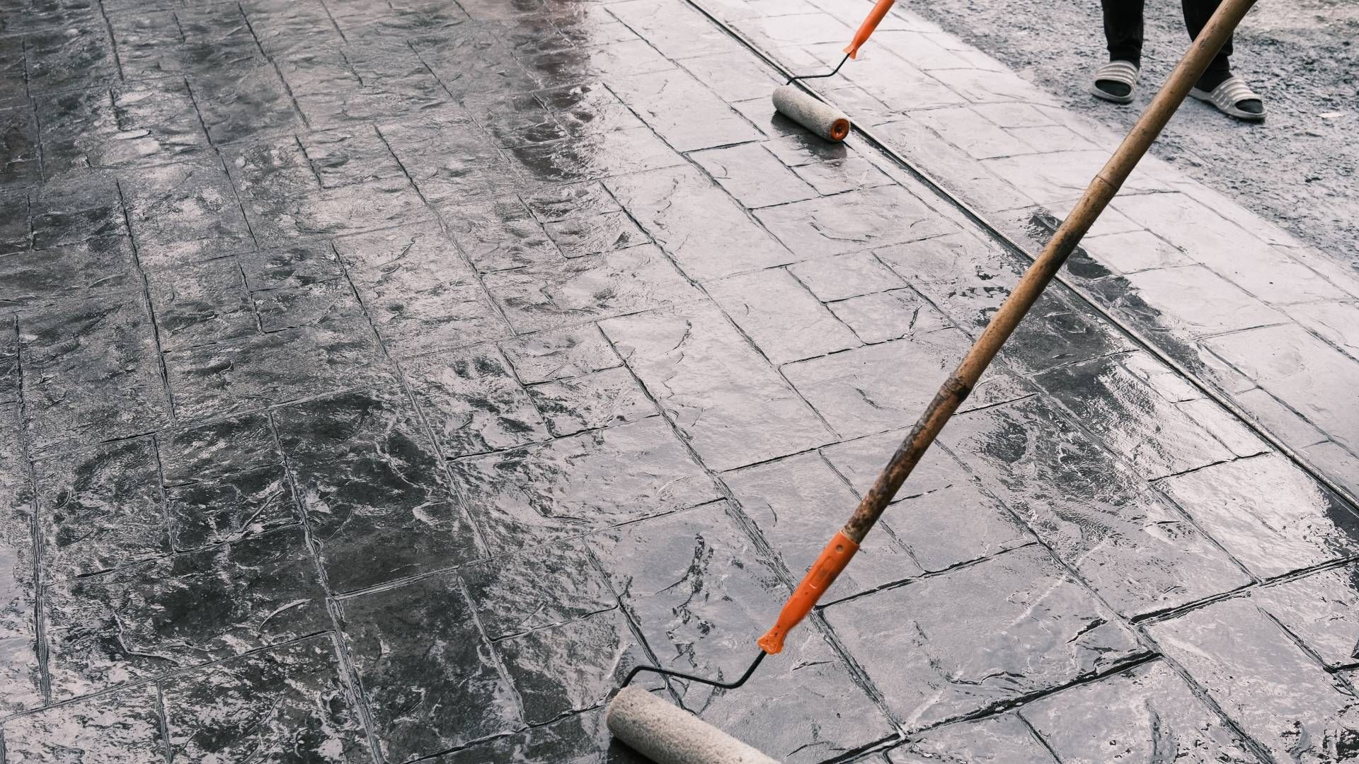 A person is painting a concrete floor with a roller.