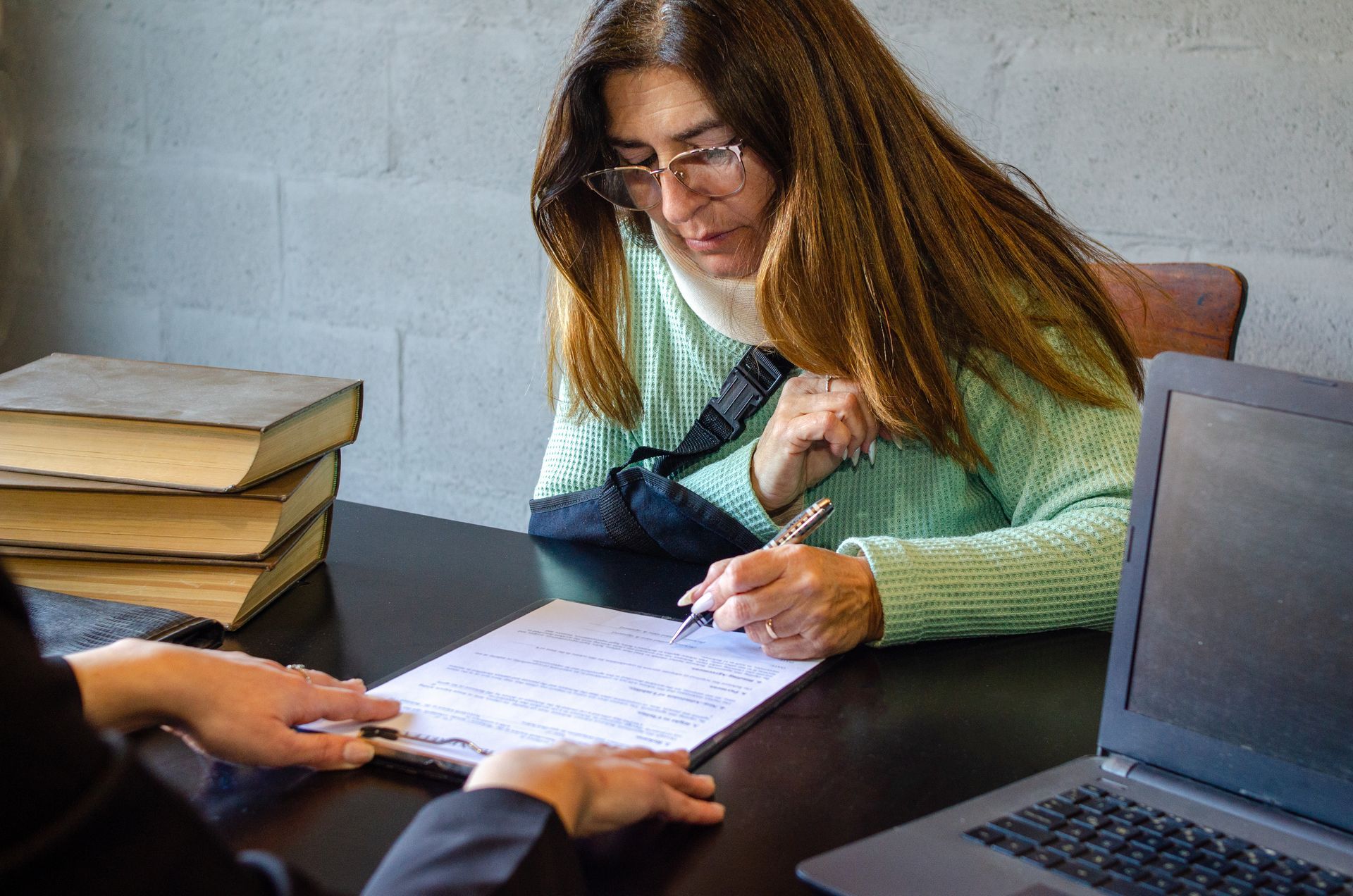 Woman reviewing paperwork at a desk with books and a laptop nearby Woman reviewing paperwork at a desk with books and a laptop nearby