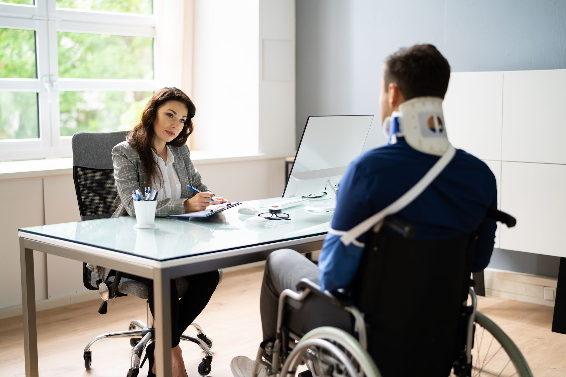 A social security disability lawyer meeting with a client in a wheelchair at an office desk. A social security disability lawyer meeting with a client in a wheelchair at an office desk.