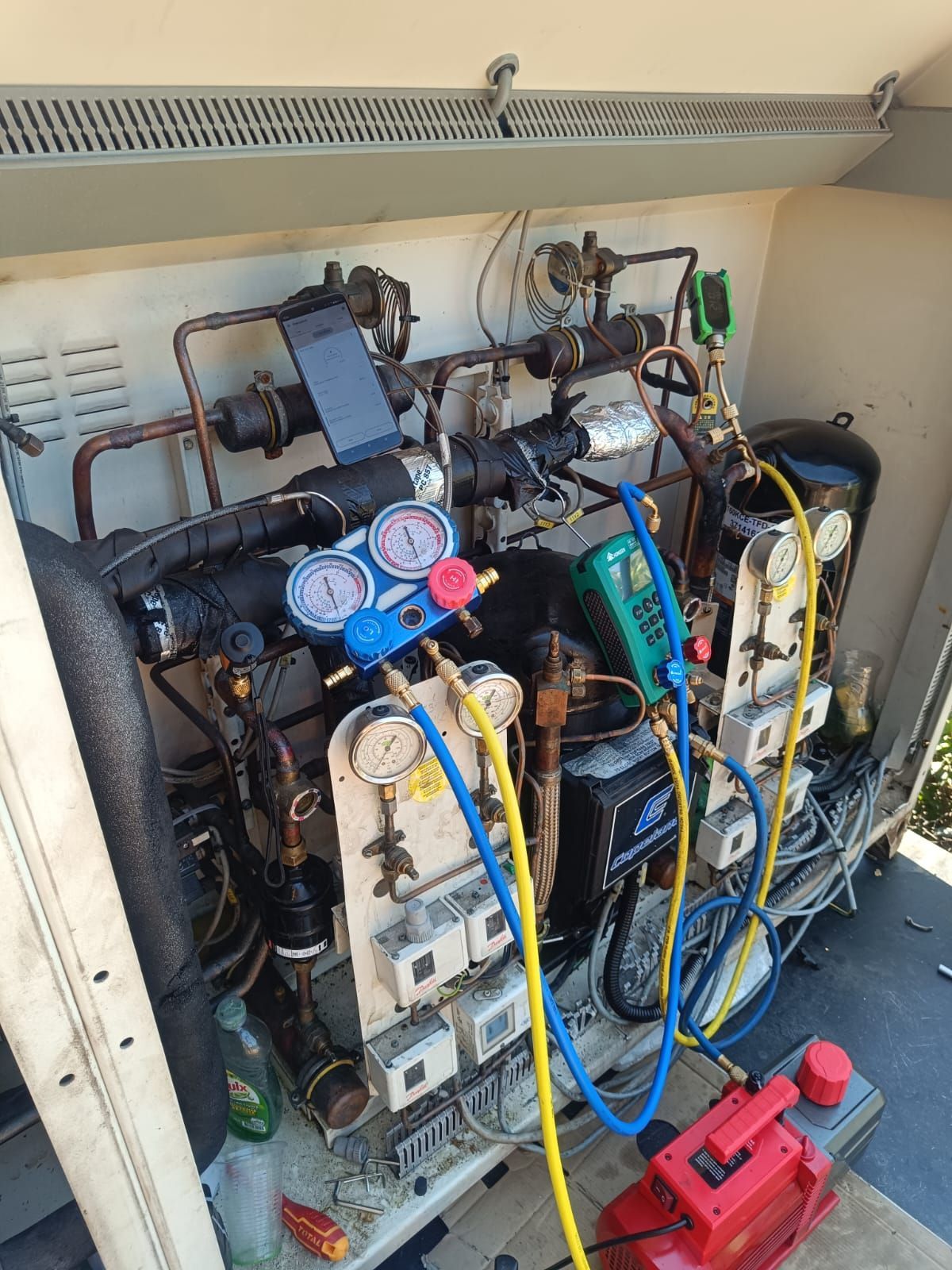 Colector de servicio eléctrico de climatización con mangueras azules y amarillas conectadas a los equipos, además de una bomba de vacío roja en un área de servicio.