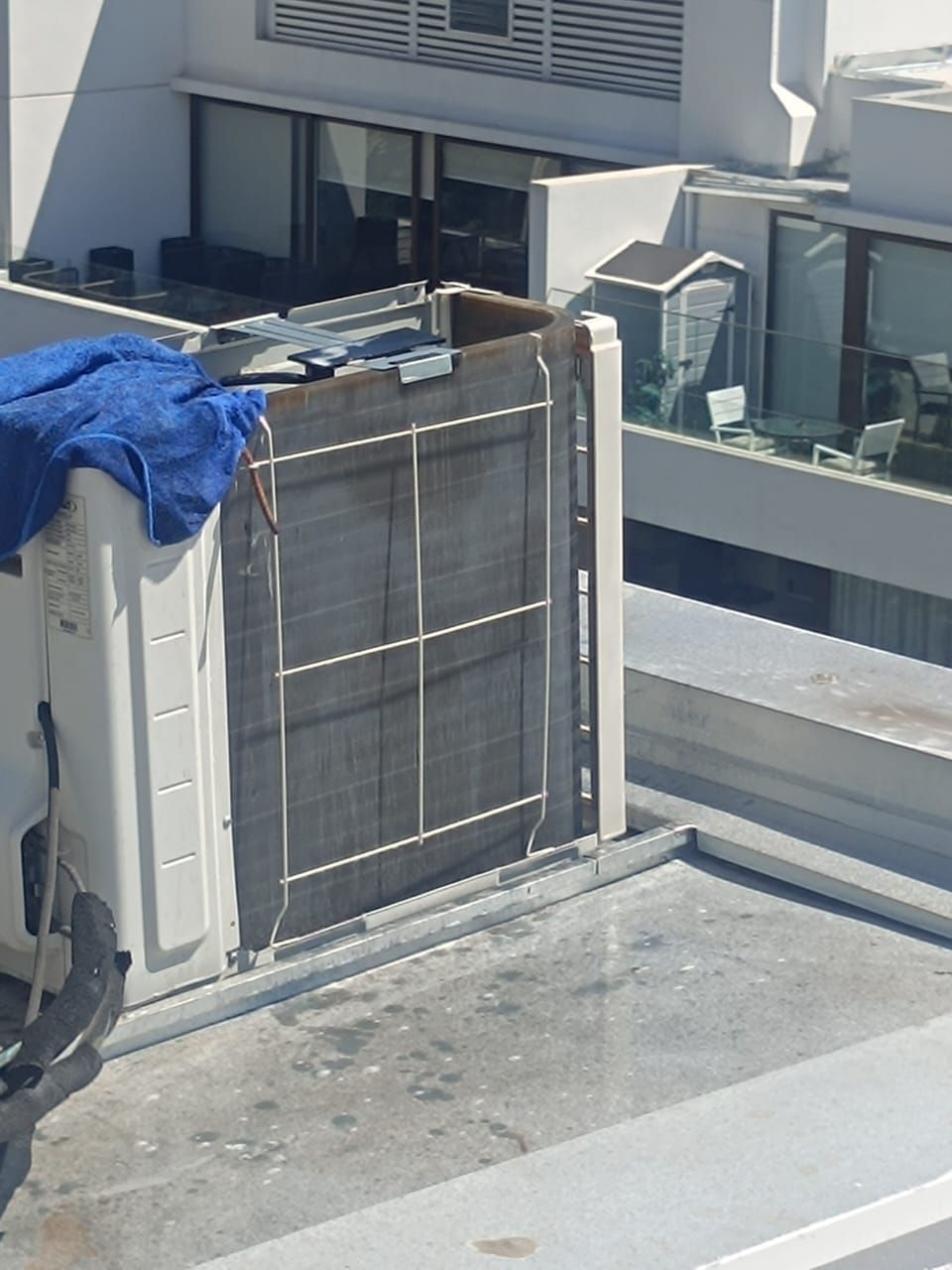 Unidad de climatización exterior en la azotea cubierta con una lona azul junto a la cornisa de un edificio.