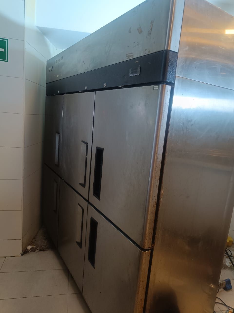 Congelador de cocina comercial de acero inoxidable con doble puerta en una esquina alicatada.