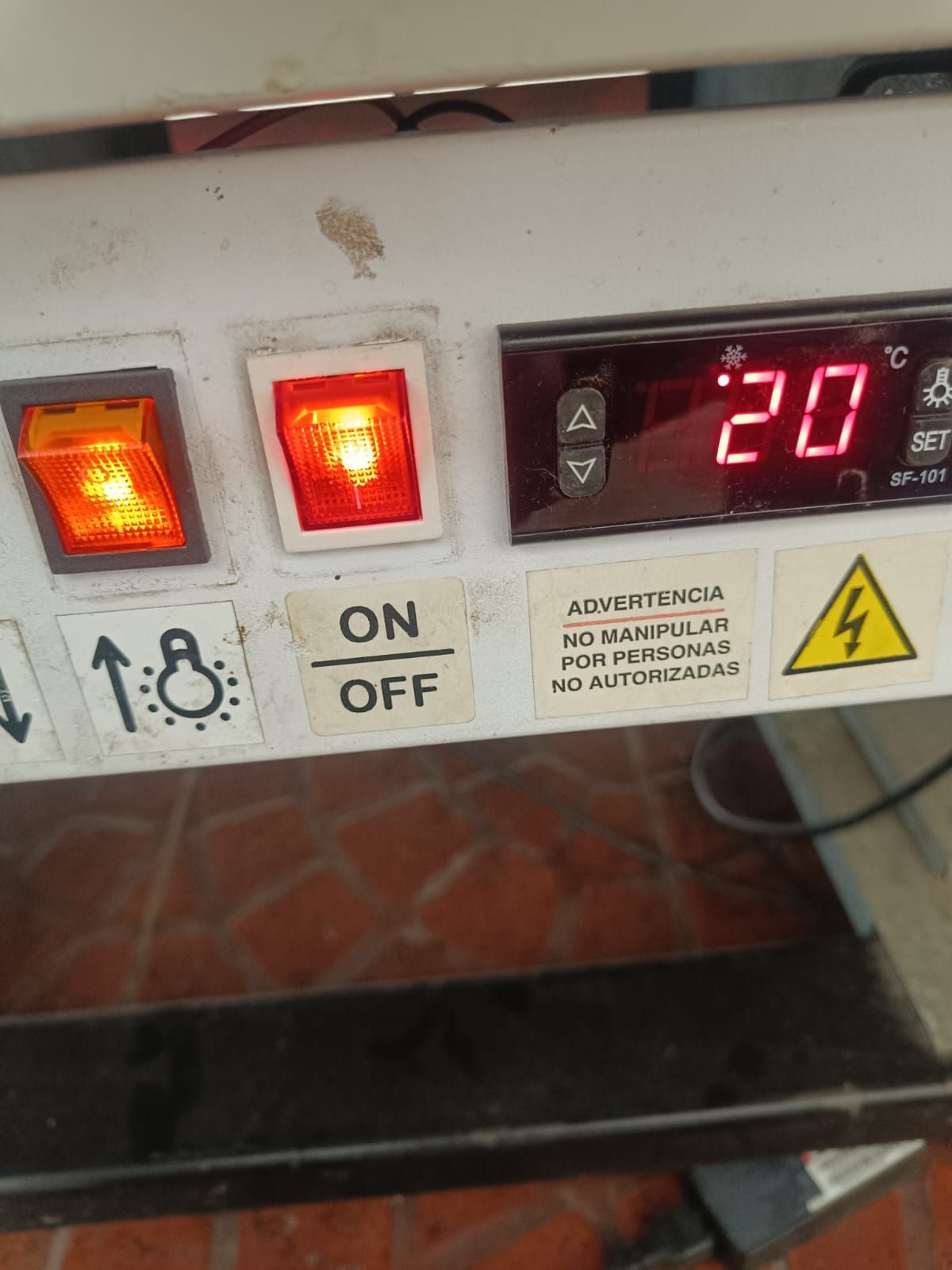 Panel de control con indicadores rojos luminosos y una pantalla digital que muestra el número 20, además de un interruptor de encendido/apagado y un símbolo de advertencia.
