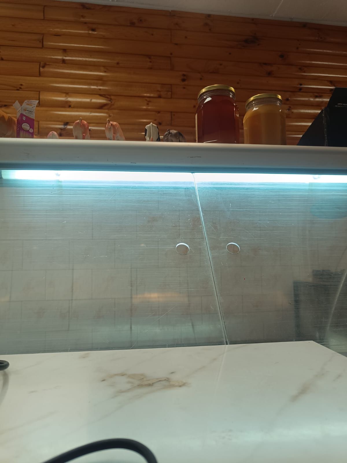 Cocina con paneles de madera, vitrina iluminada, tarros encima y encimera blanca debajo.