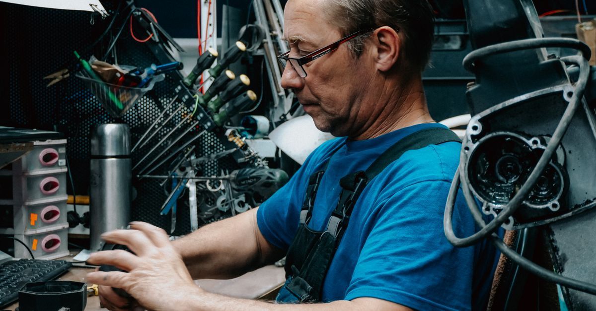 Técnico con camisa azul trabajando en piezas de bicicleta en un taller, centrado en reparaciones.