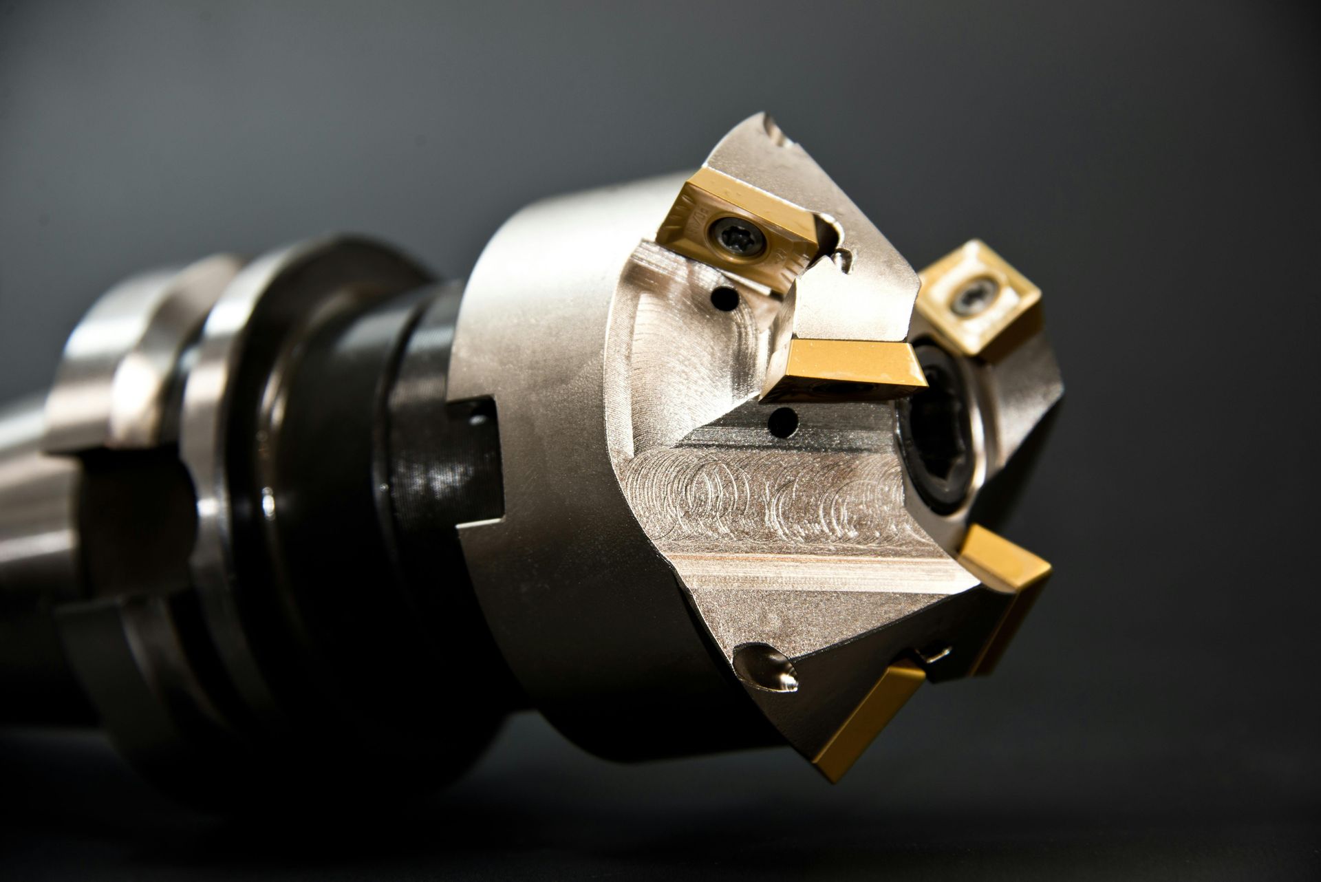Metal milling cutter with gold inserts, against a dark background.