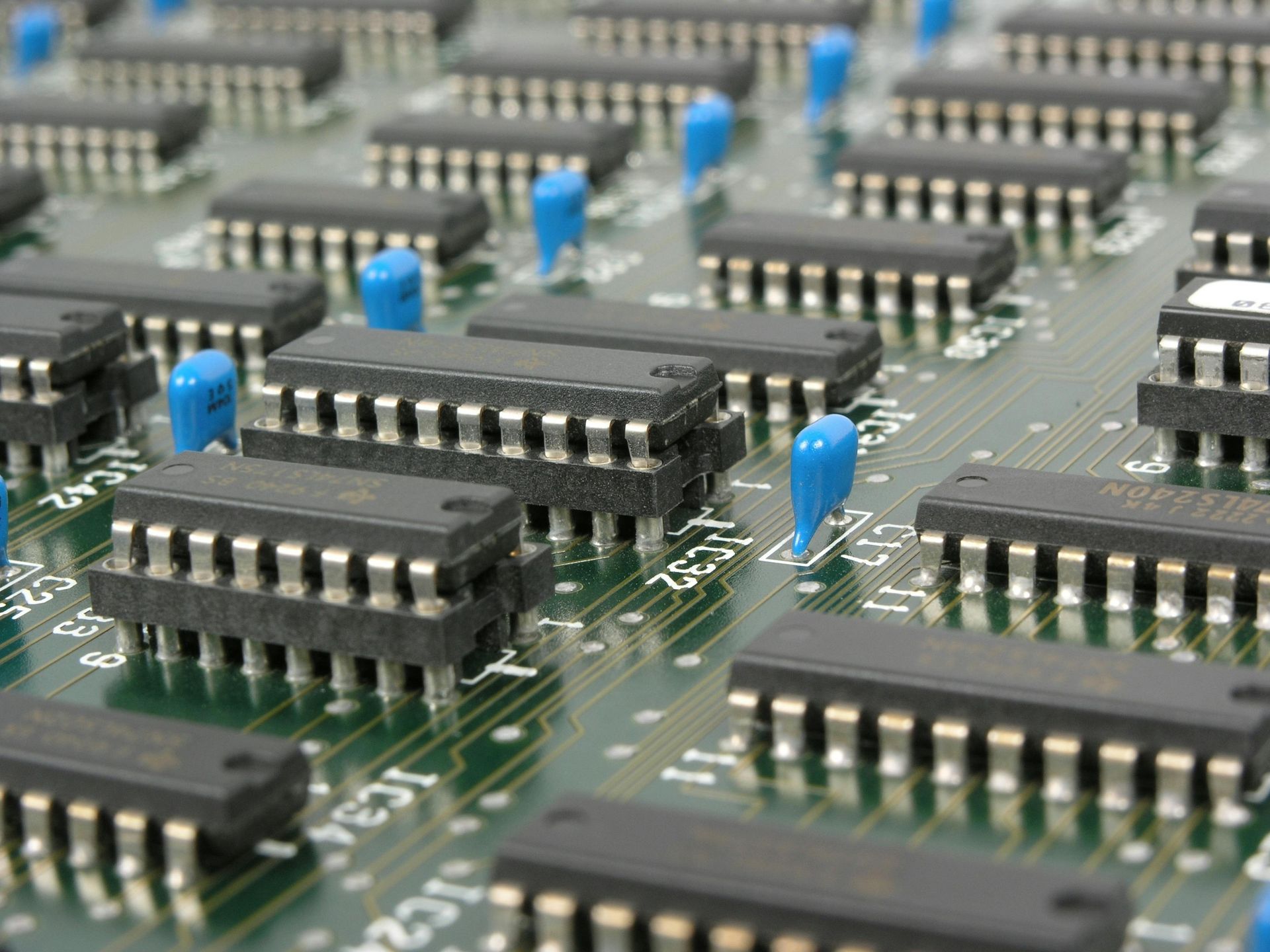 Close-up of a circuit board densely populated with black integrated circuits and blue capacitors.