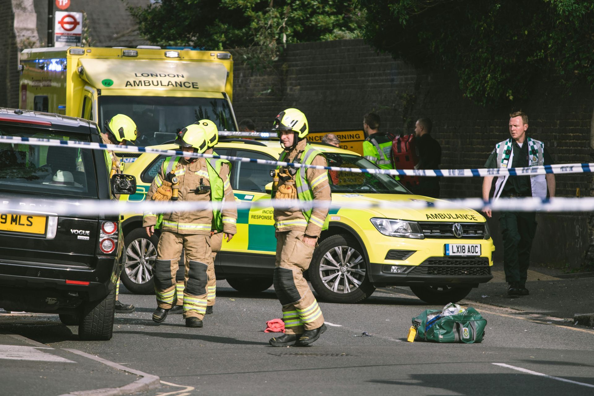 Emergency responders at a street scene with fire trucks, ambulance, and barrier tape.