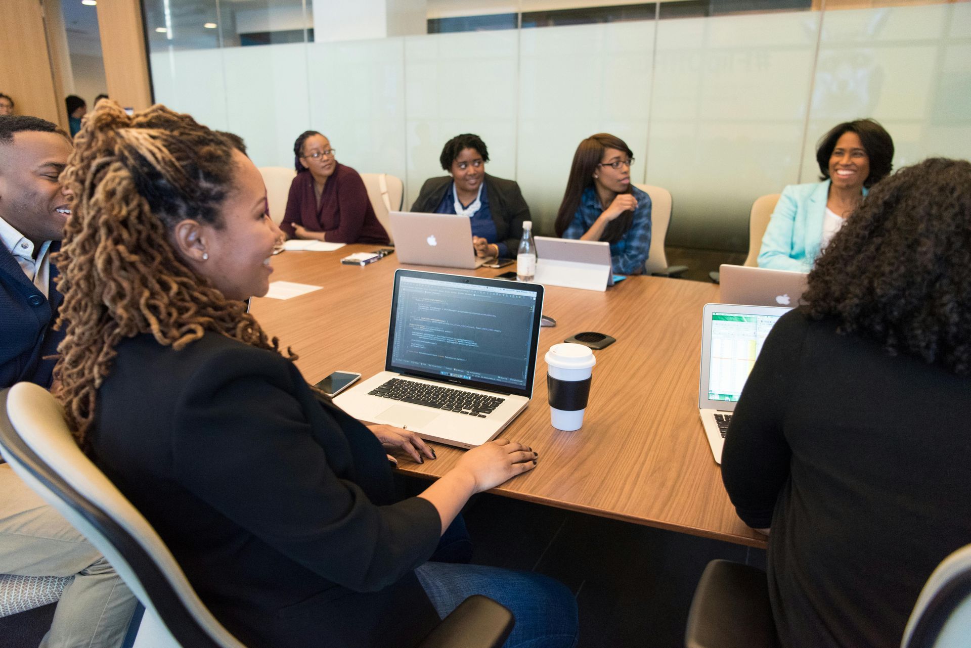 Group of Black professionals in a meeting, seated at a table with laptops and coffee.