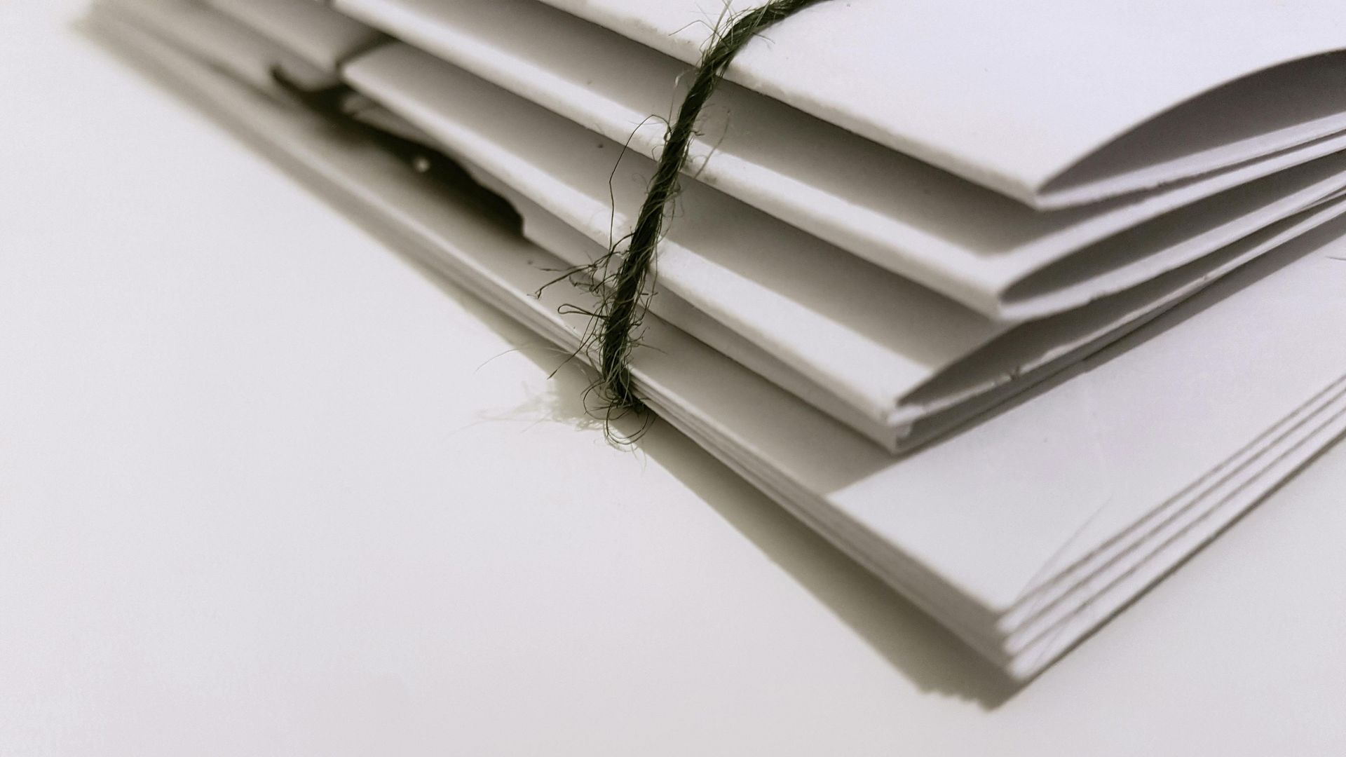 Stack of white paper tied with a dark green string on a white surface.