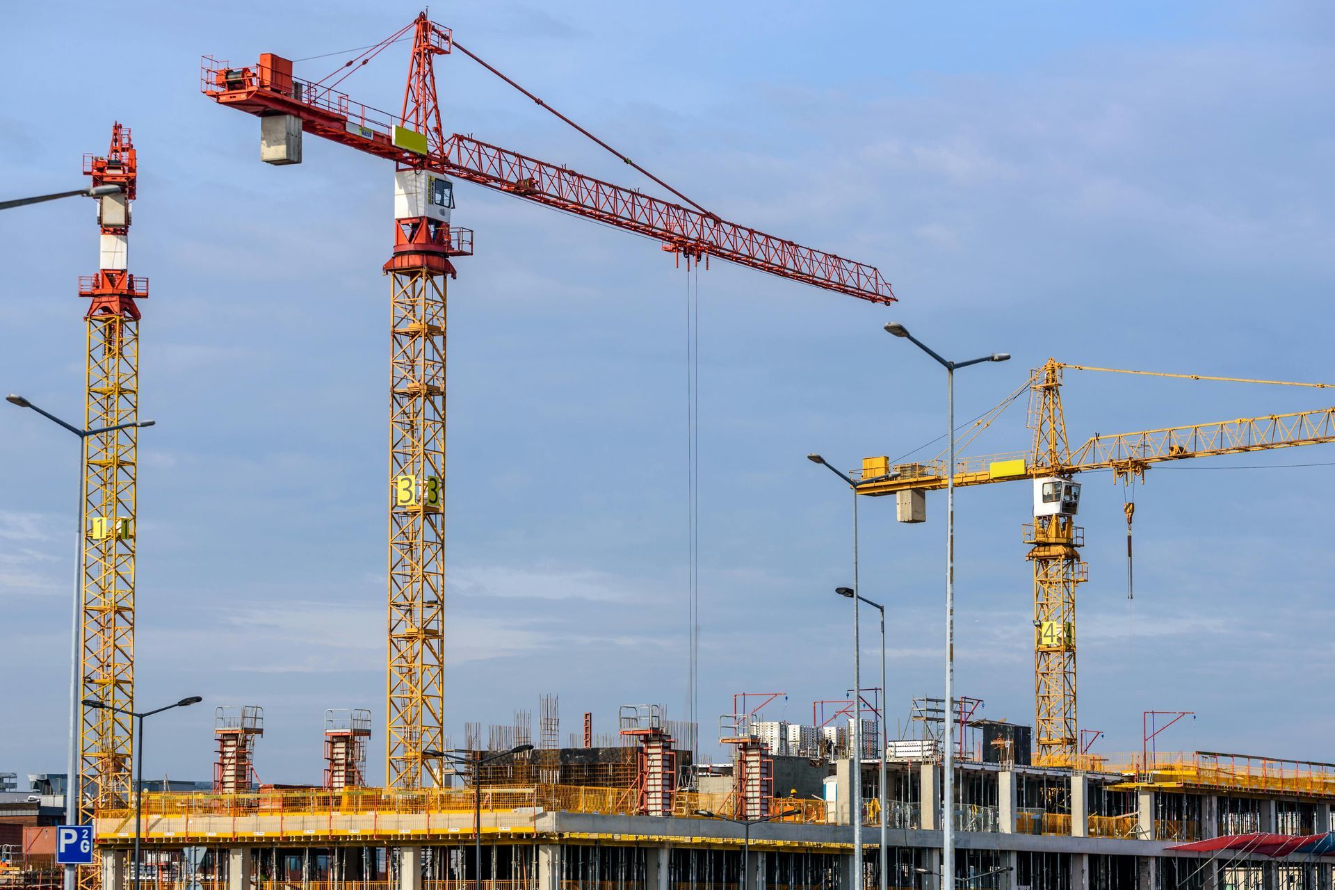 Construction site with red and yellow cranes against a cloudy sky.