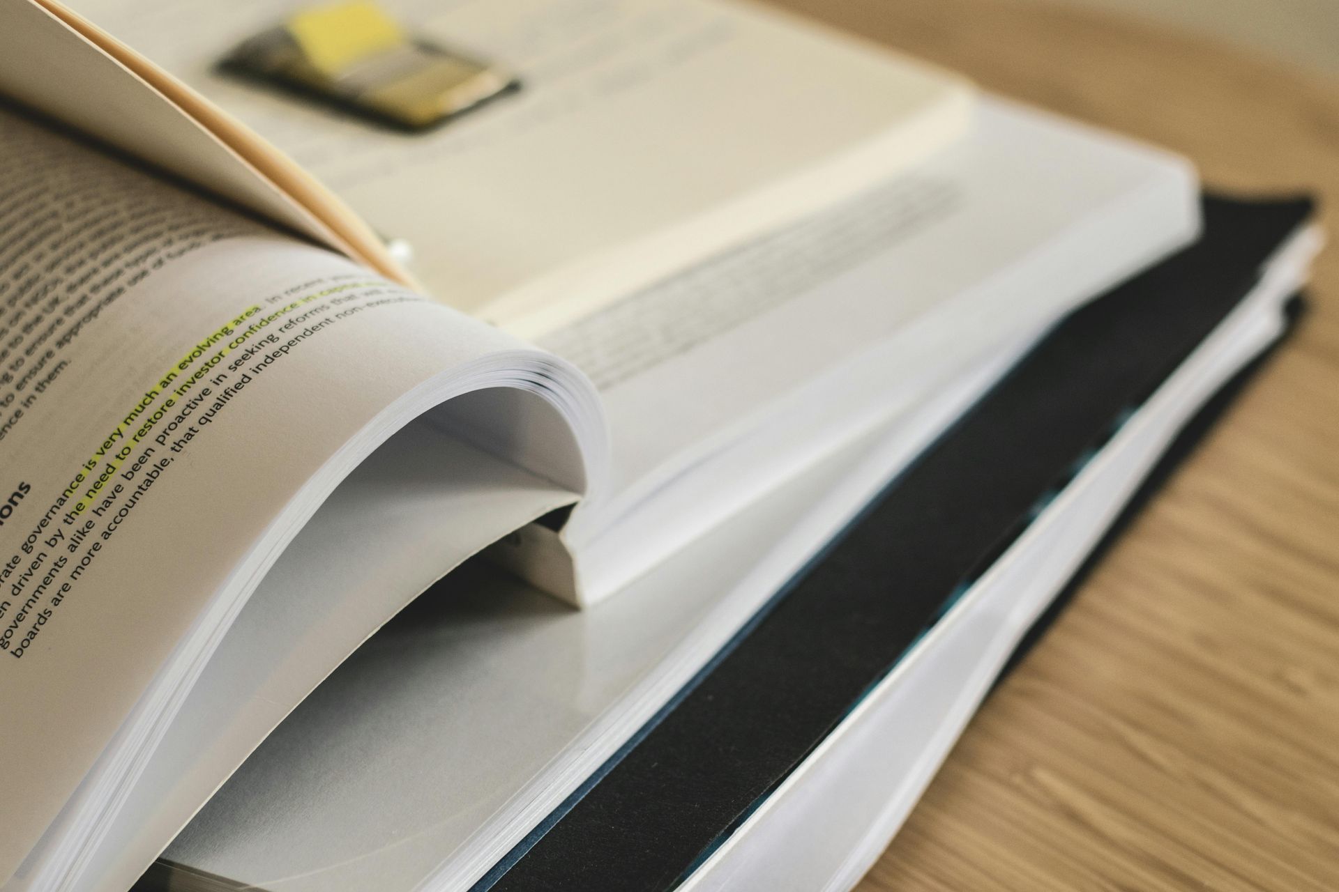 Pile of open books on a wooden surface; pages highlighted with a yellow marker and a sticky note.