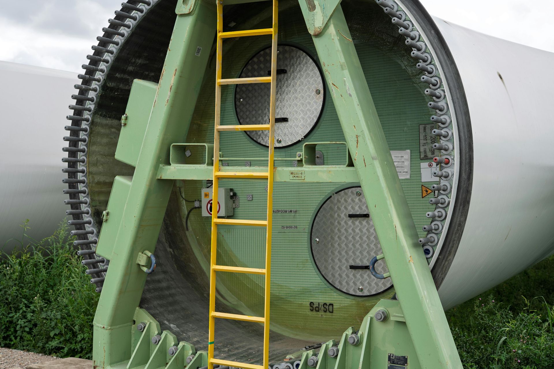Green wind turbine component with ladder inside, mounted on a support frame.