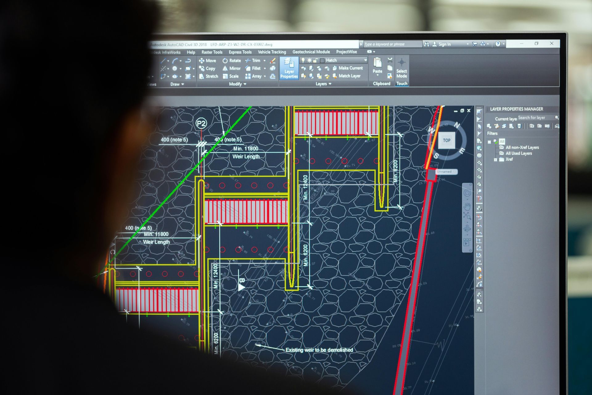 Person looking at a computer screen with a technical drawing of a construction plan in progress.