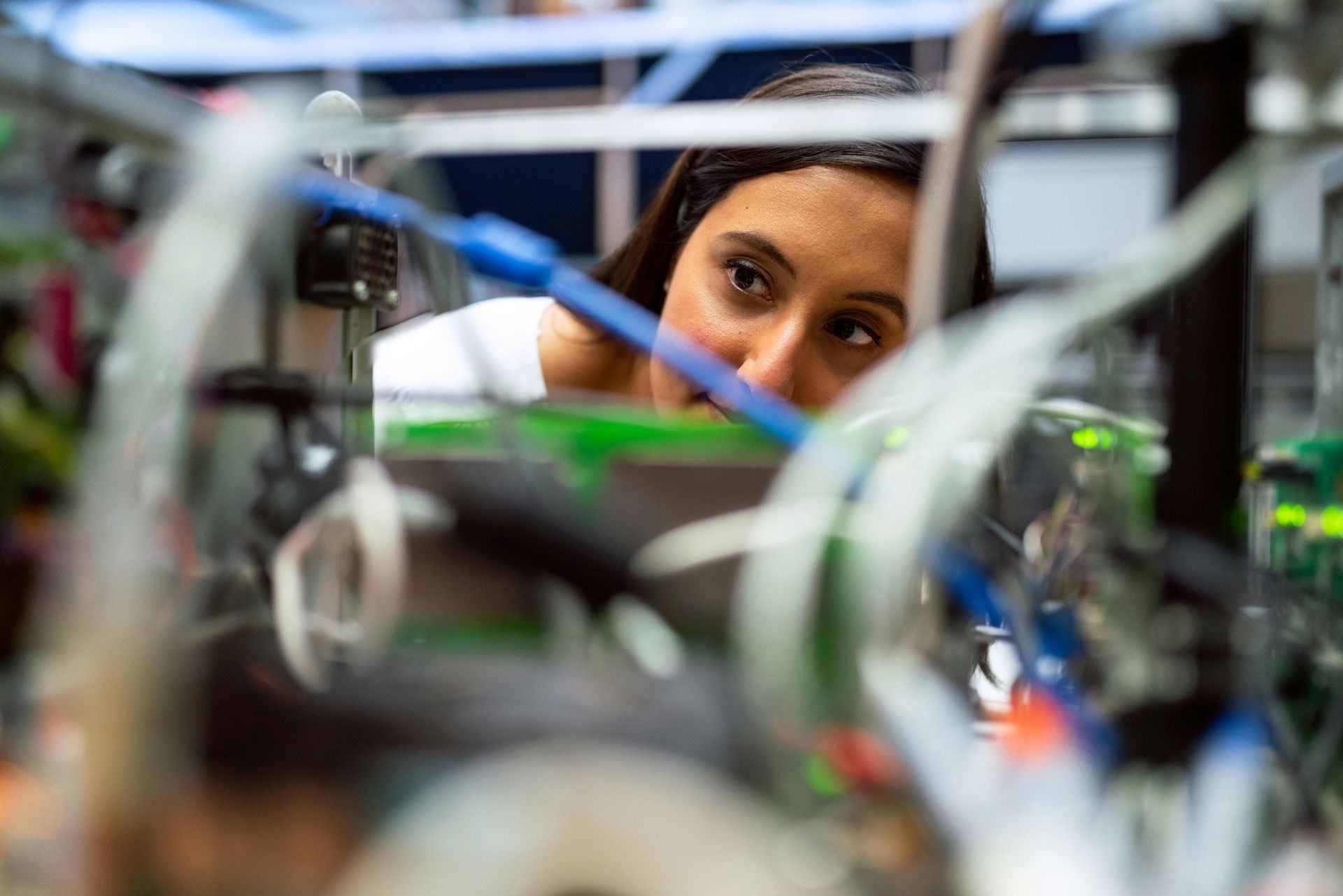Woman focused on complex machinery, examining wires and components in a lab setting.