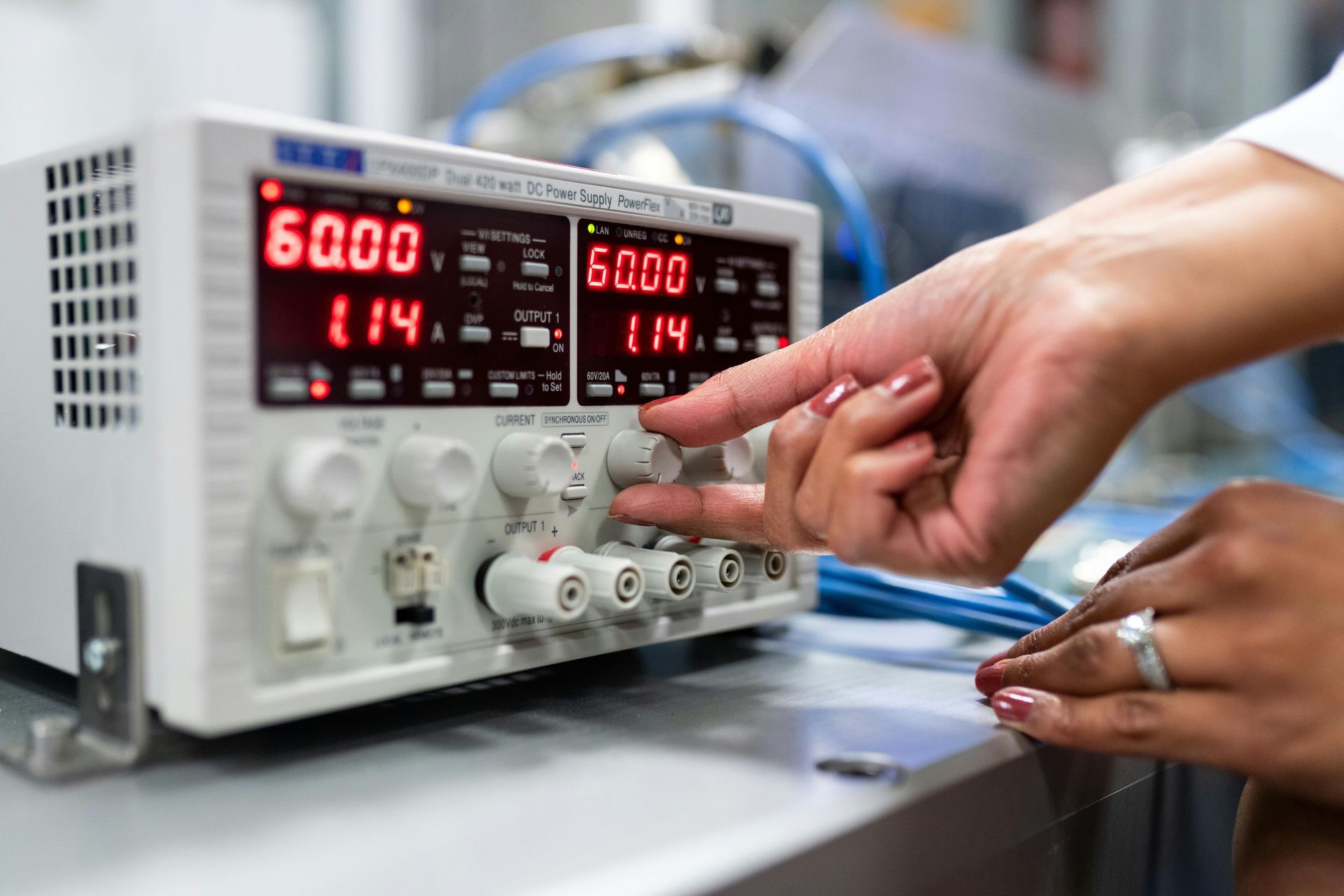 Person adjusting a power supply, showing red digital displays for voltage and current.