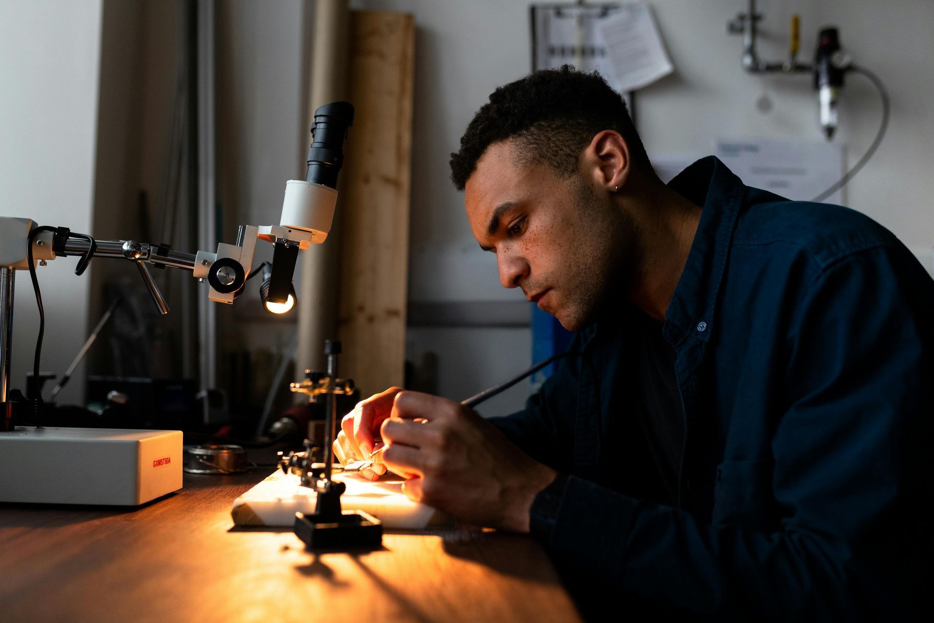Man using tools, working on a small object under a microscope in a workshop, focused.