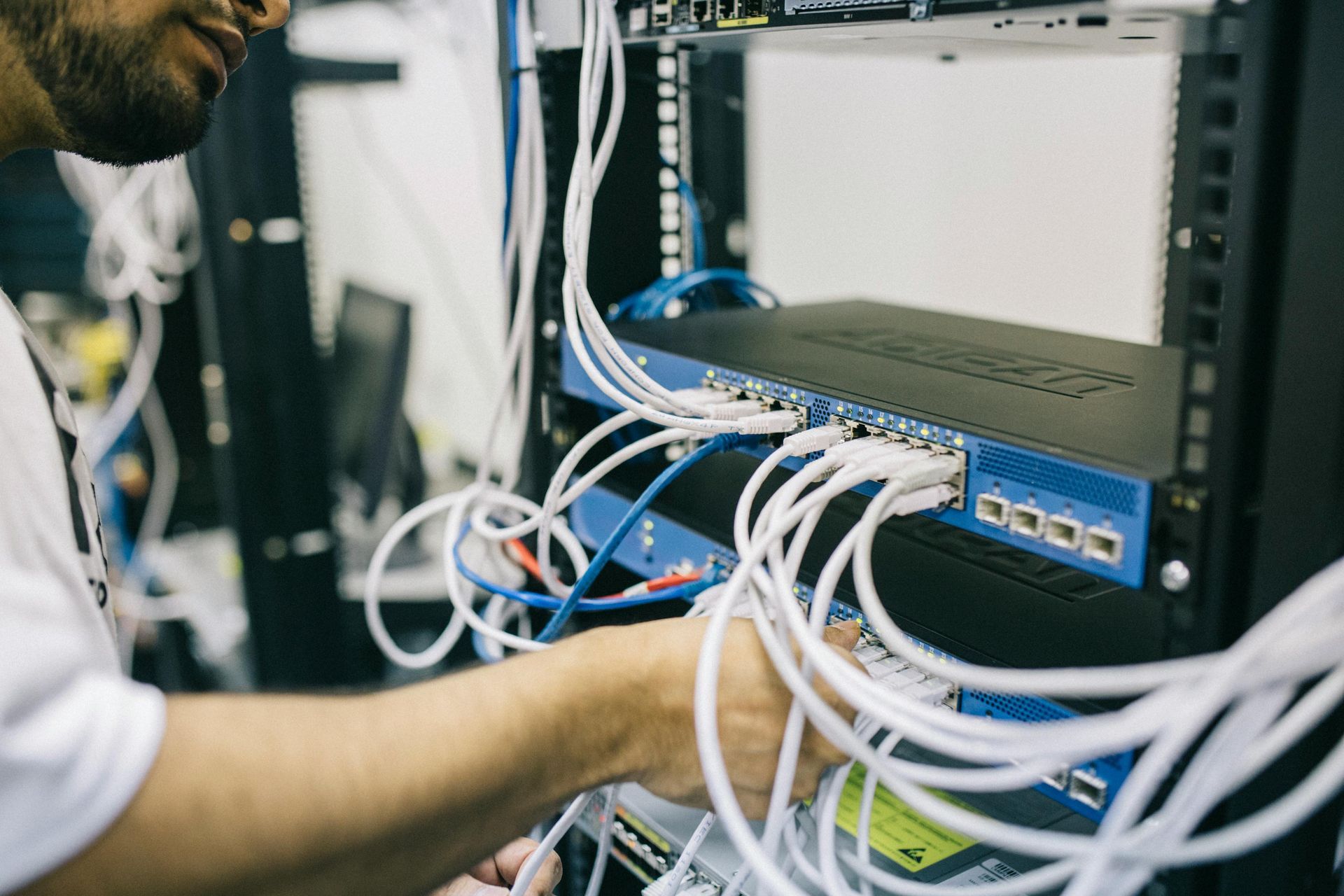Person working on a network server rack, connecting white cables to blue devices.