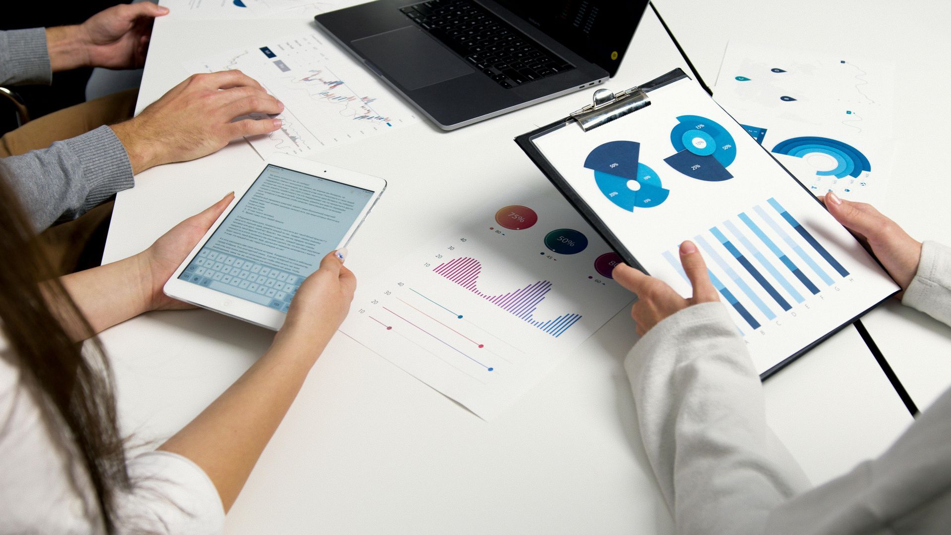 Business team analyzing charts and graphs around a table with laptop and tablet.