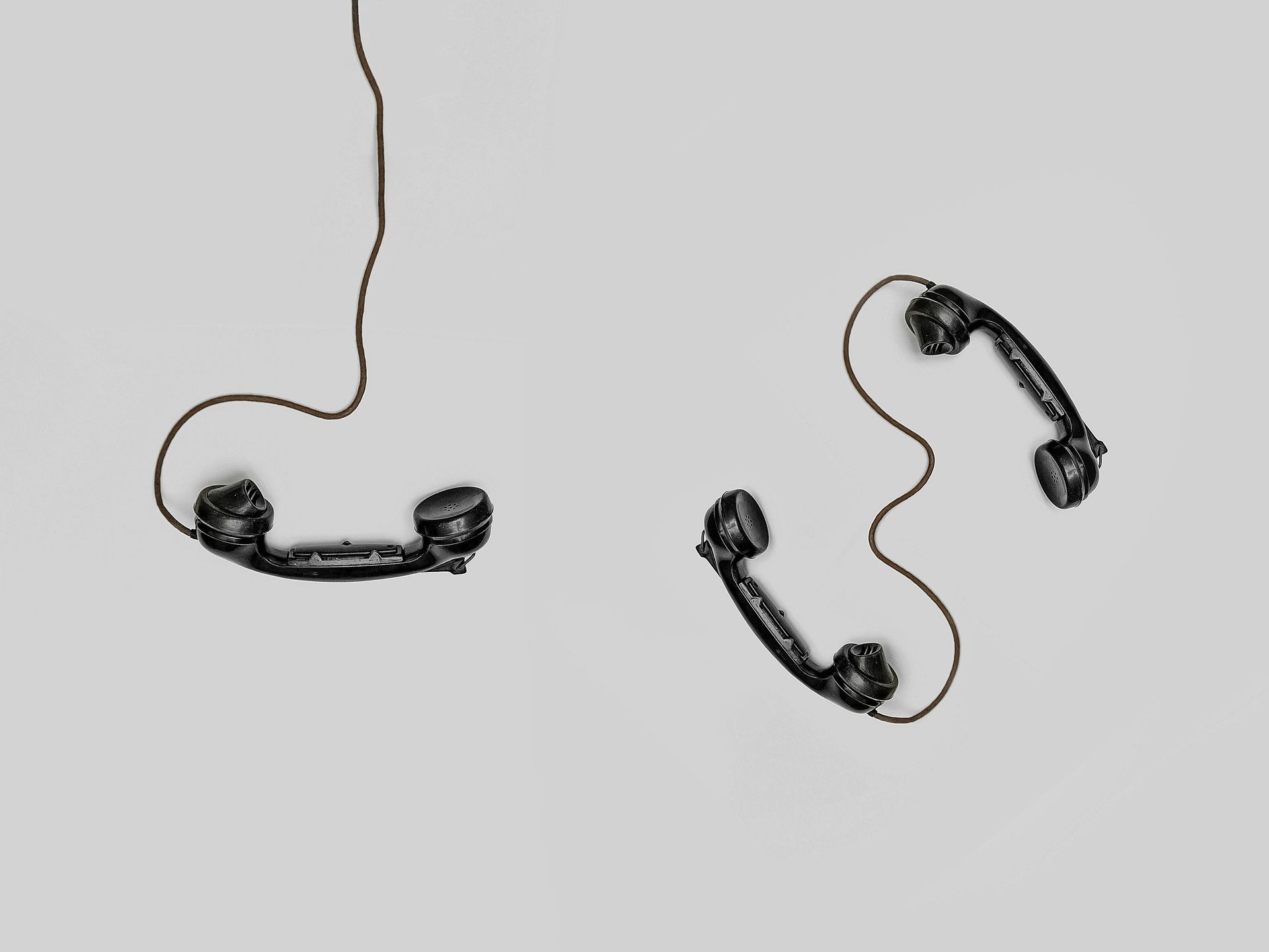Two black vintage telephone handsets and cords, on a light gray background.