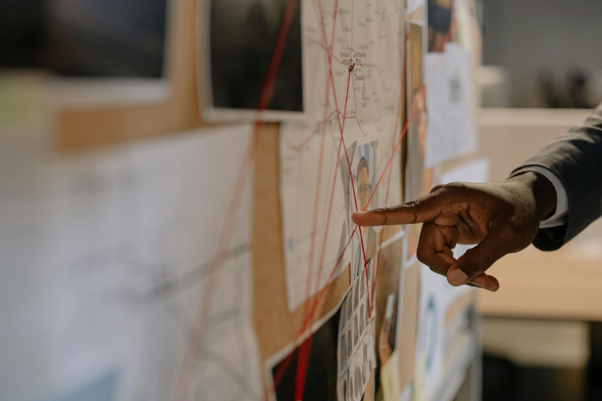 A Black hand pointing at a crime scene investigation board with photos and connected strings.